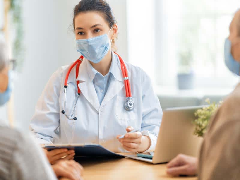 physician wearing mask speaking with two older patients