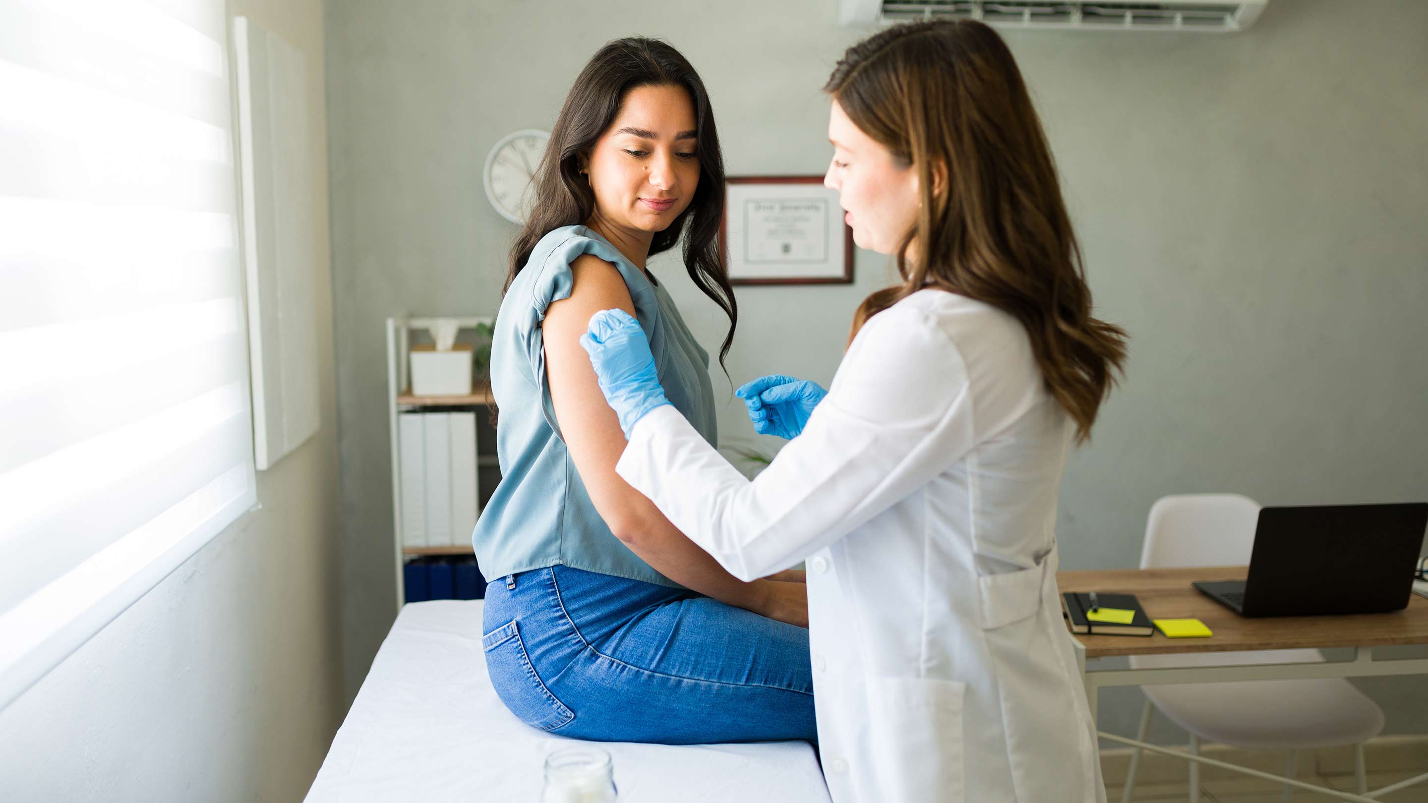 Young hispanic woman getting vaccinated by a professional medical worker.