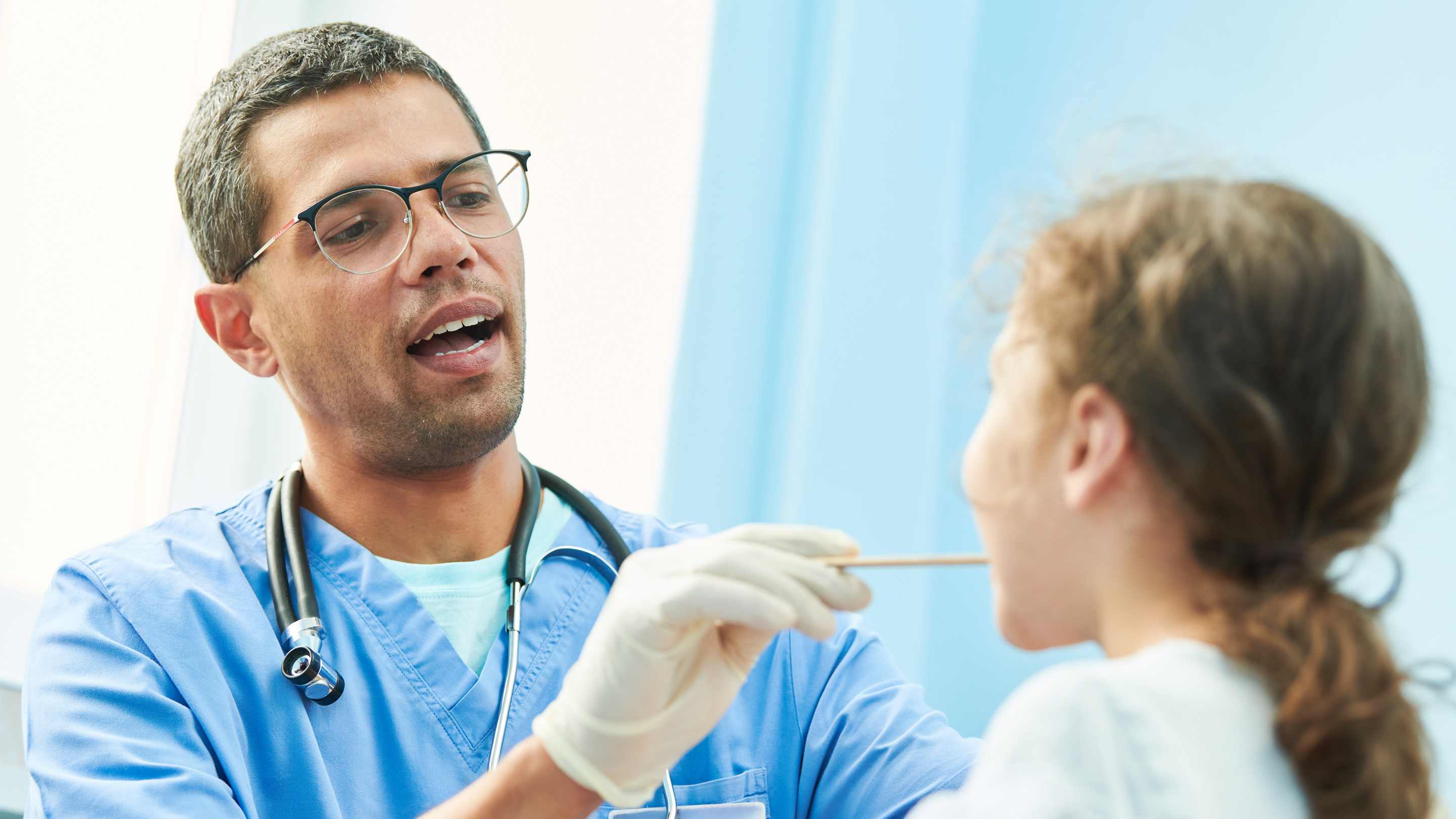 Male doctor giving a throat swab to a young female patient during an ear, nose and throat exam