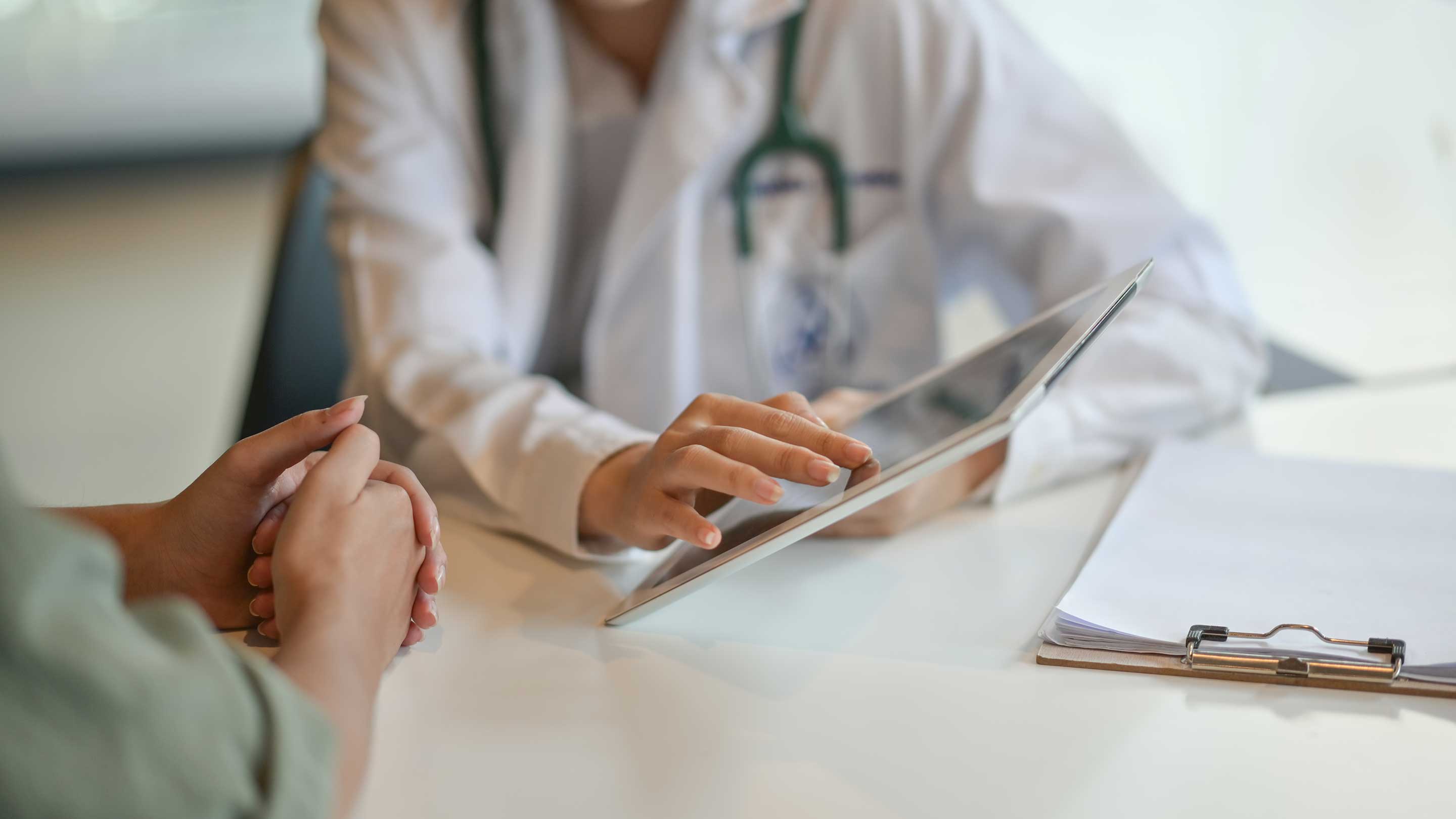 A doctor showing a patient some information on a tablet, only their hands and arms are visible.