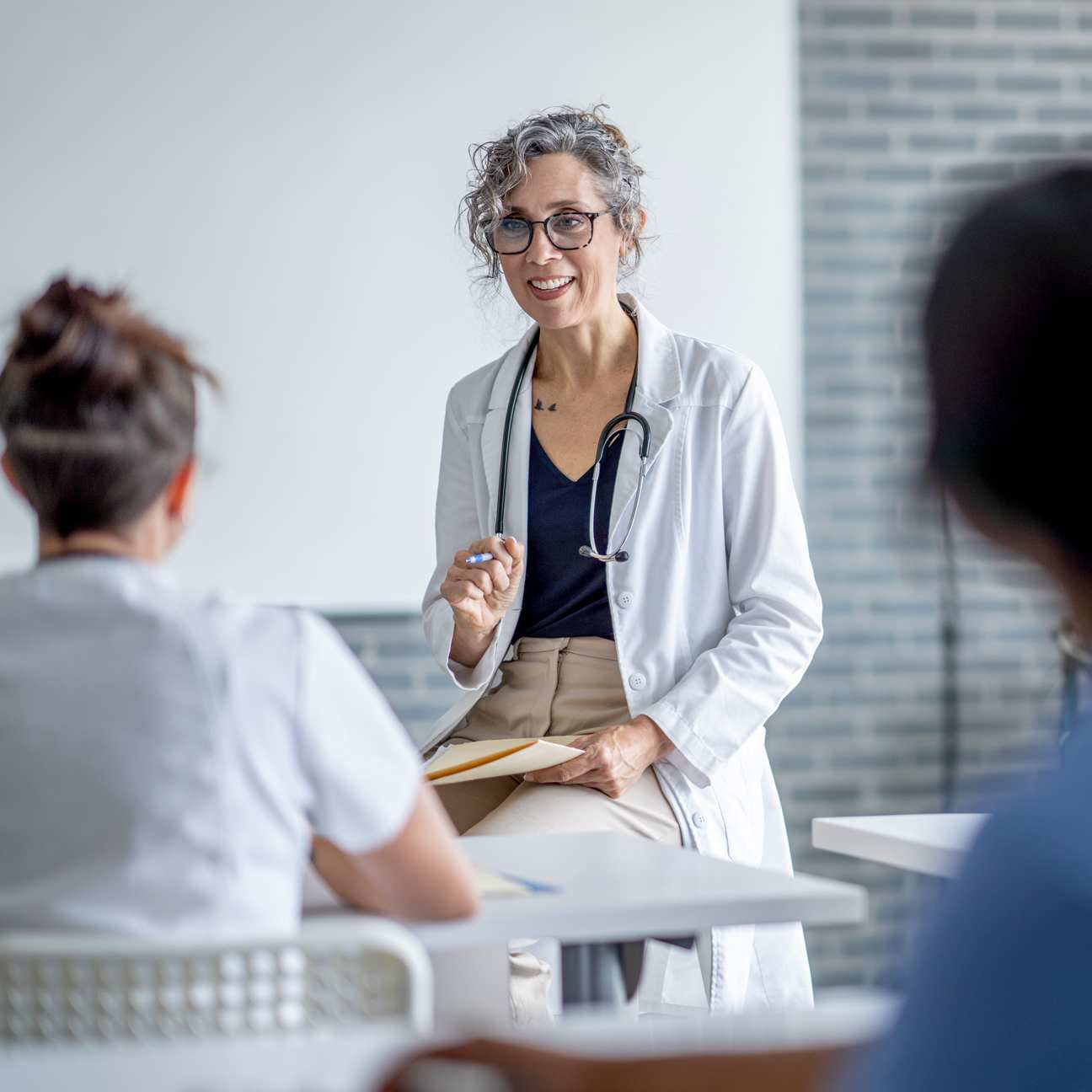 Image of a mature female physician sitting at the front of a classroom as she teaches a small group of students.