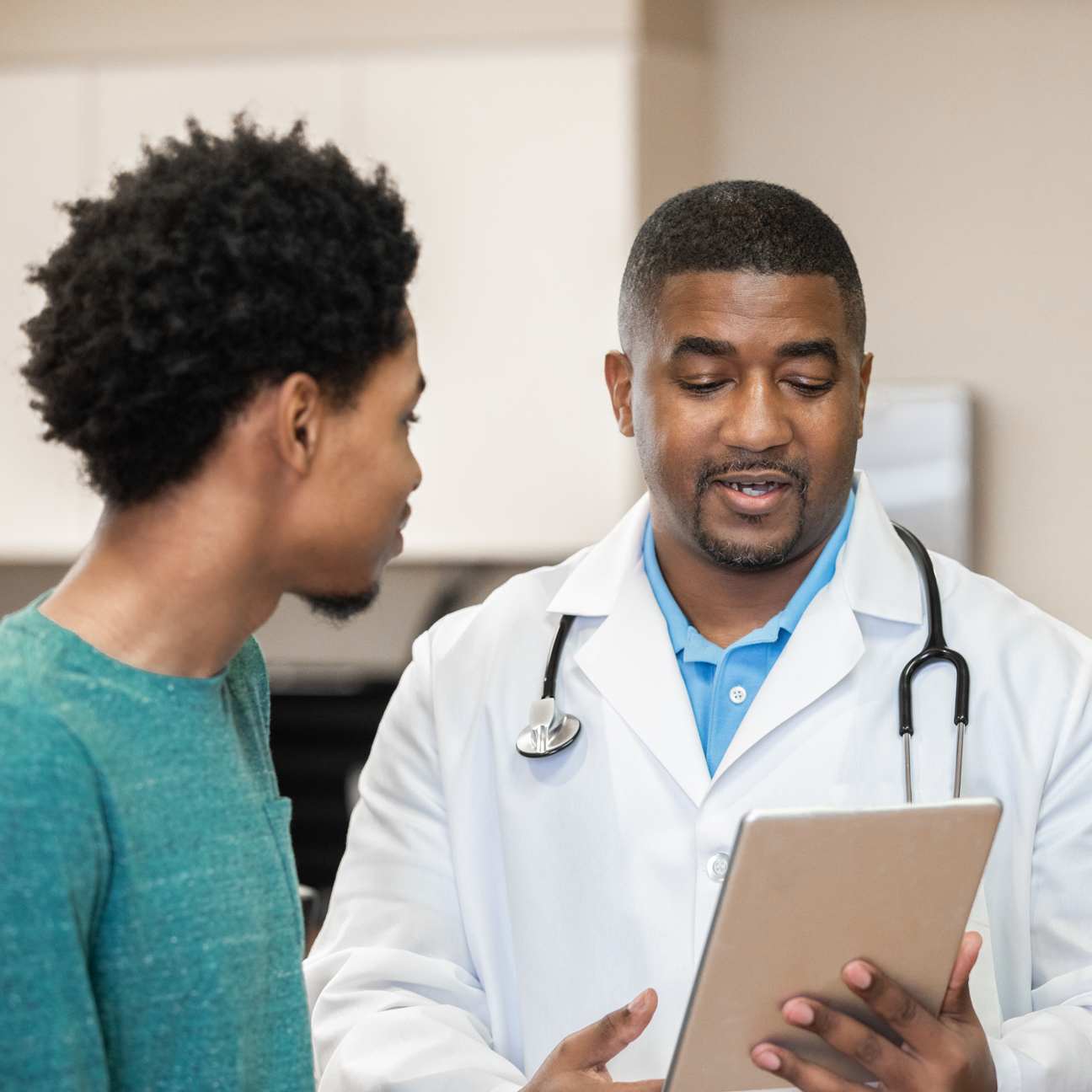 Image of a male physician holding digital tablet and discussing test results with patient.