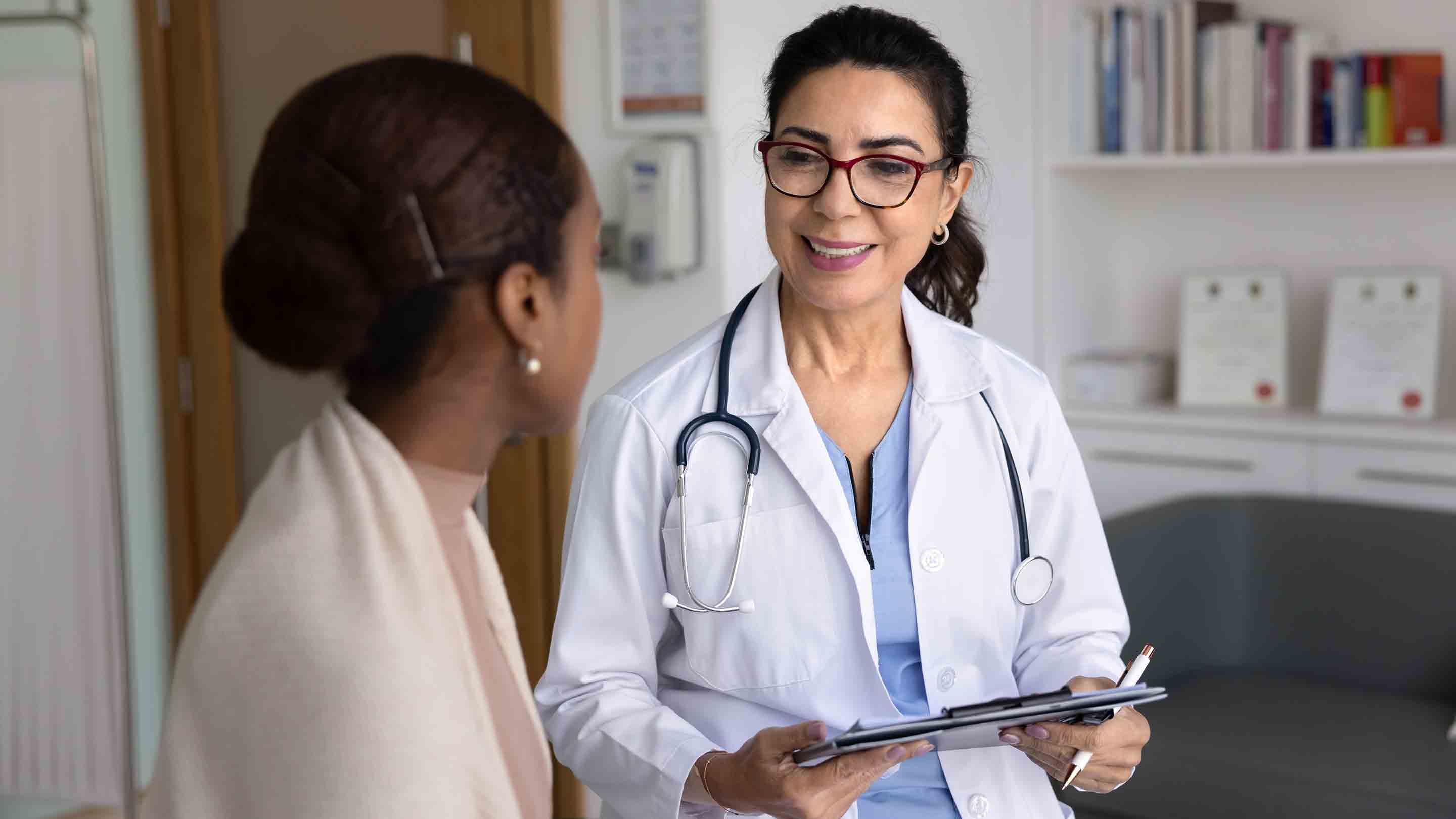 Cheerful friendly senior doctor meeting with young African patient in office.