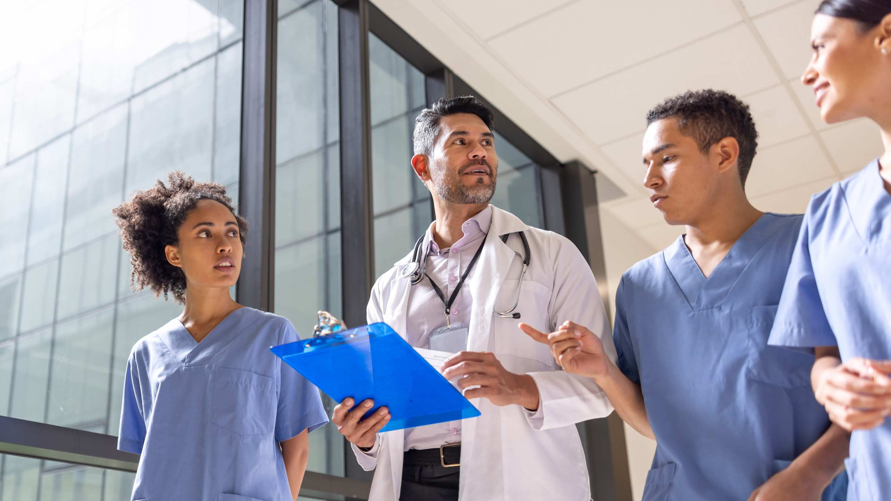 A faculty attending speaks to intern residents in the hallway of a hospital.