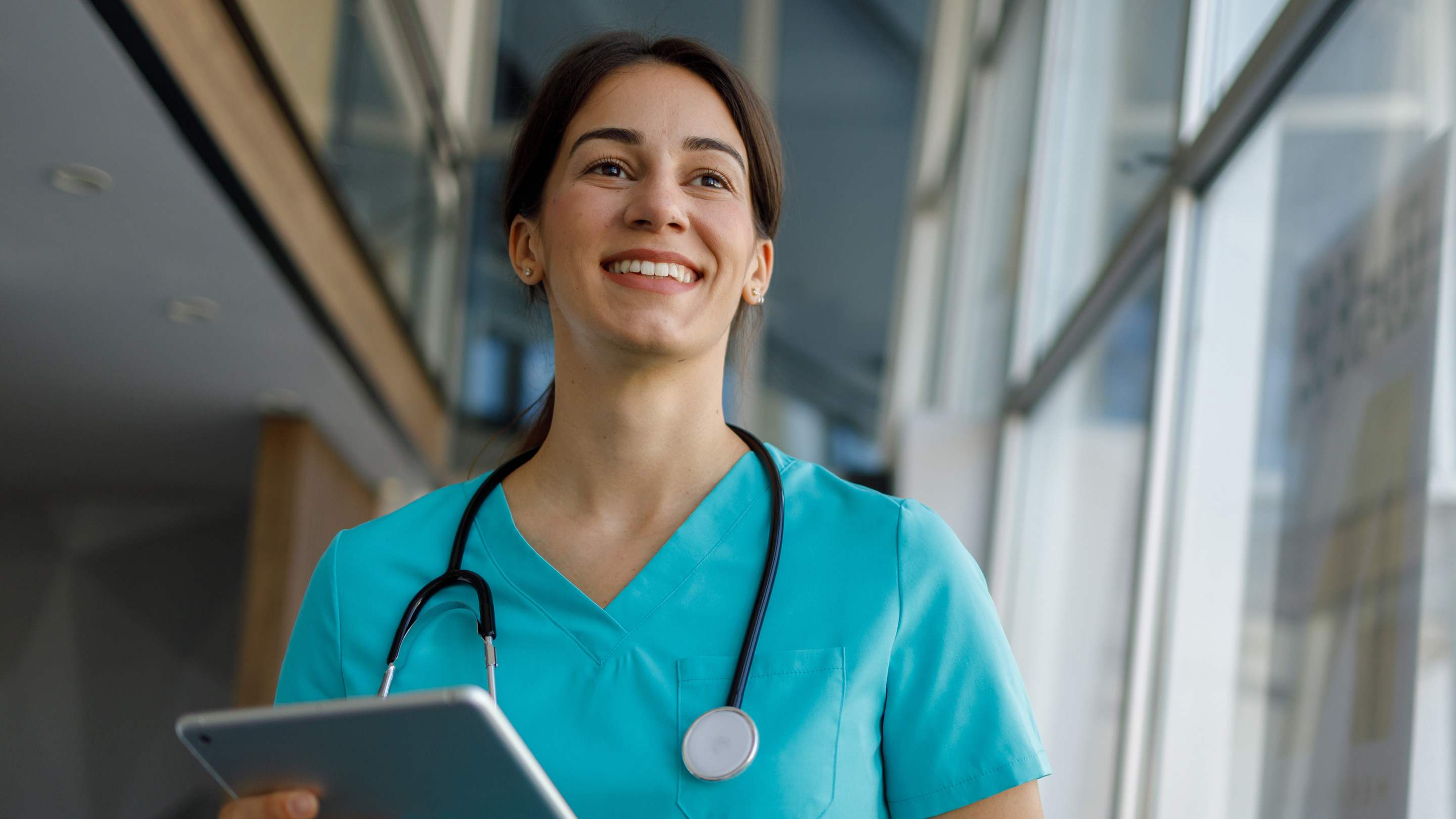 Smiling family physician walking in hospital setting with a tablet in her hand.