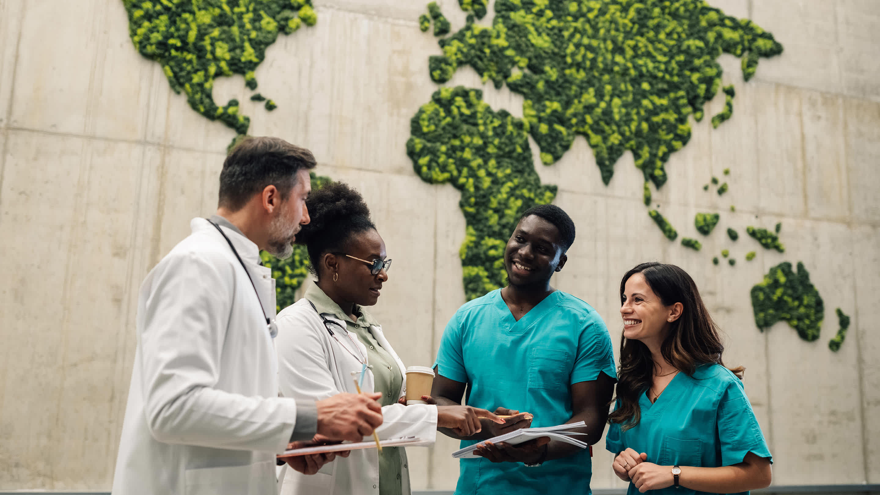 A diverse medical team has a discussion in front of a world pay made of moss.