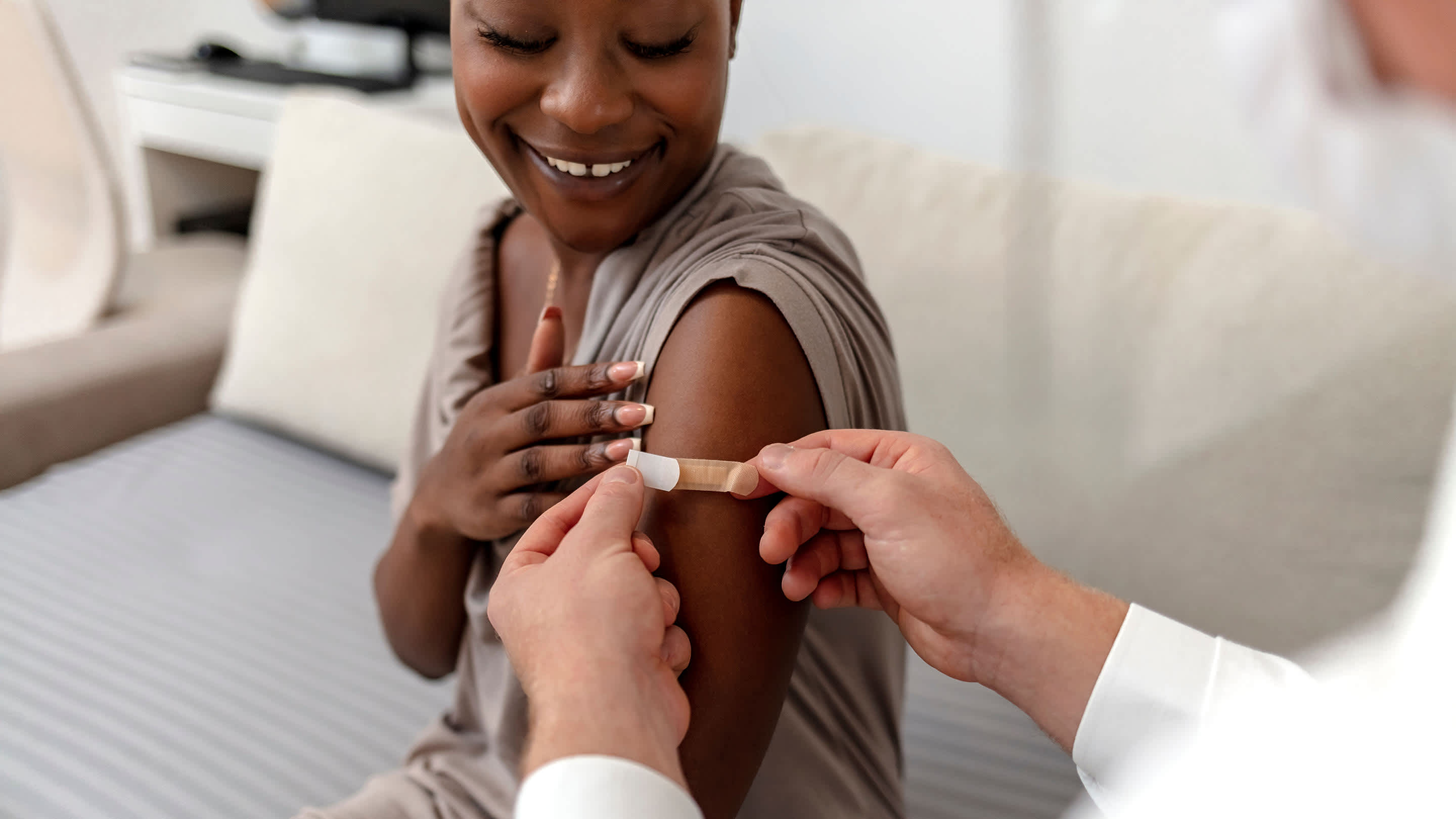 Smiling patient gets bandaid from doctor after a vaccination or blood draw.
