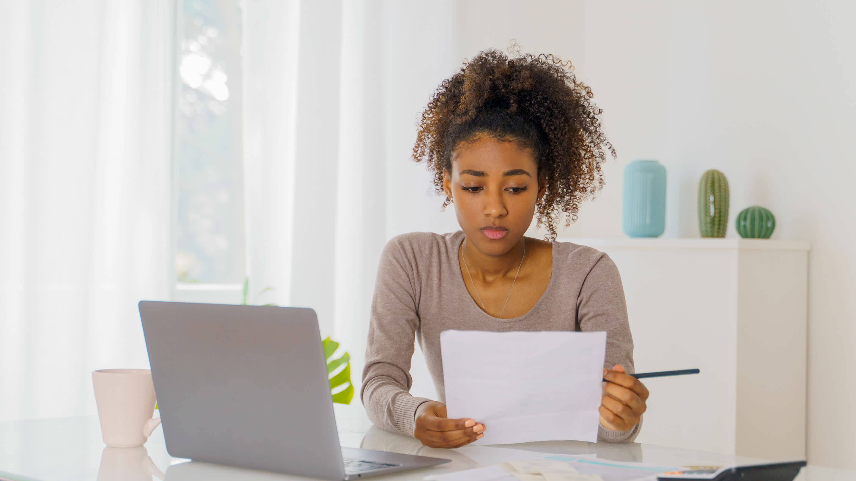 A frustrated young woman reads paperwork while seated at her desk.