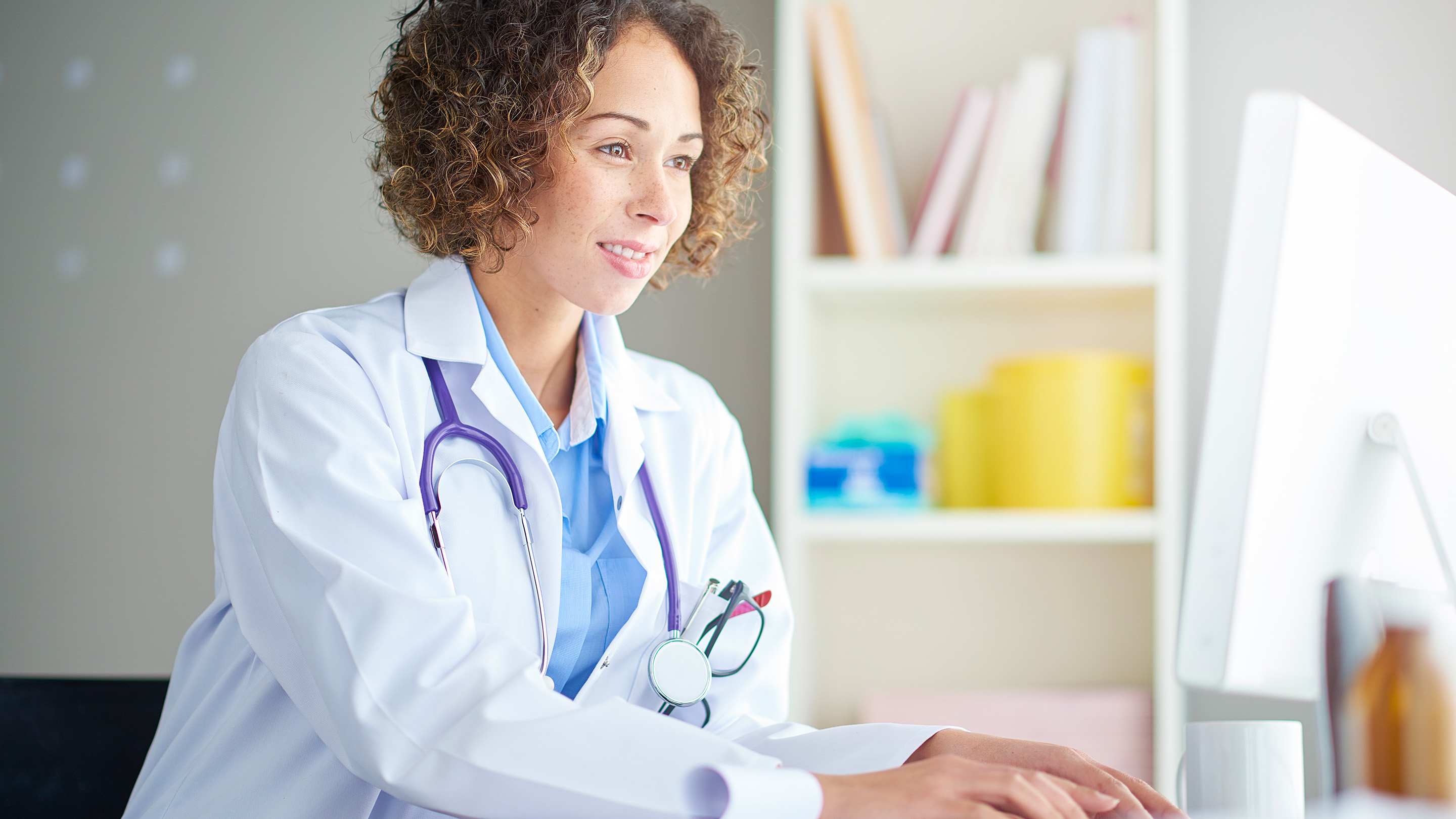 A female doctor sits at her desk and checks something on her computer.