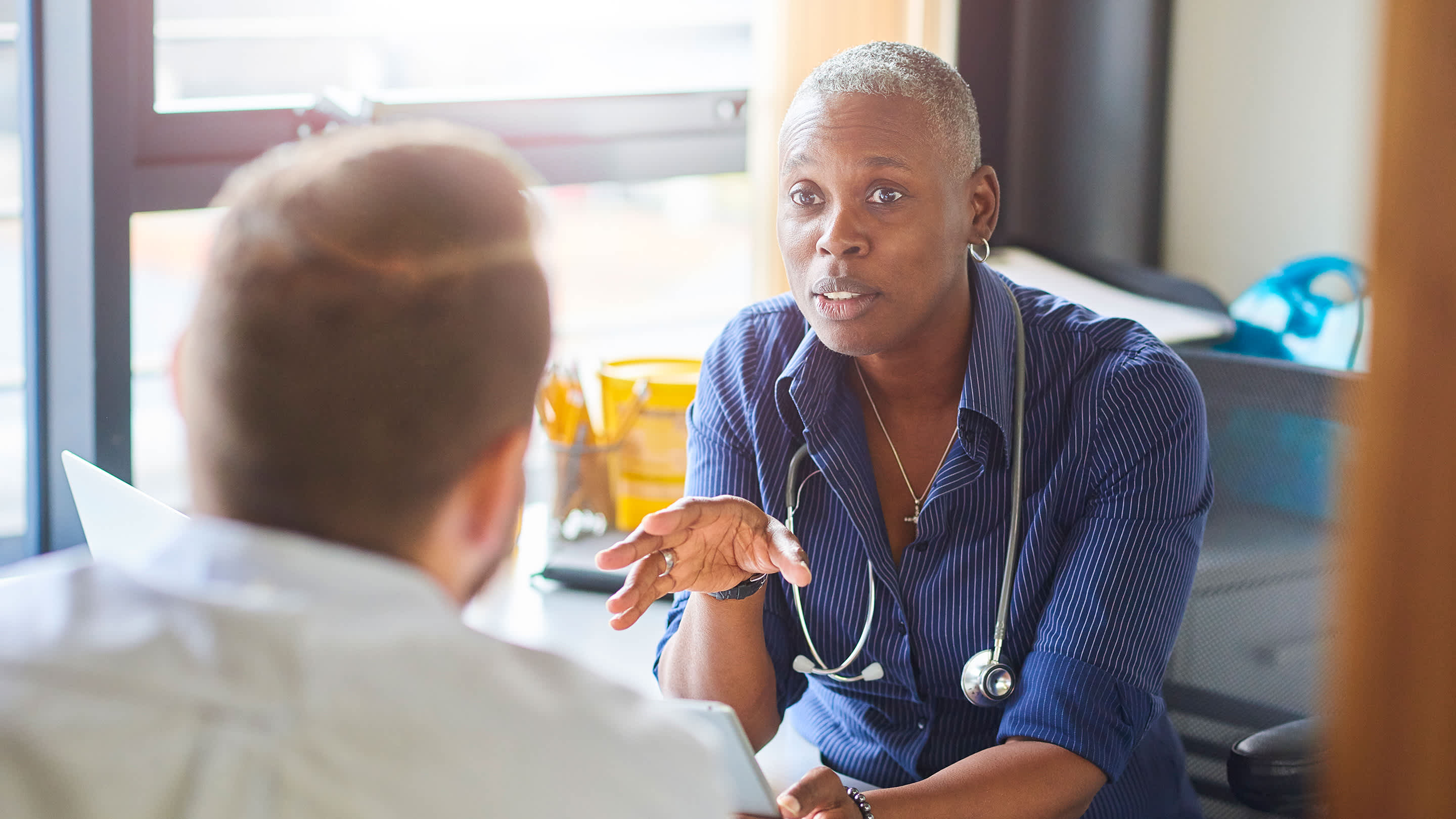 A Black female physician consults with a patient in an office setting.