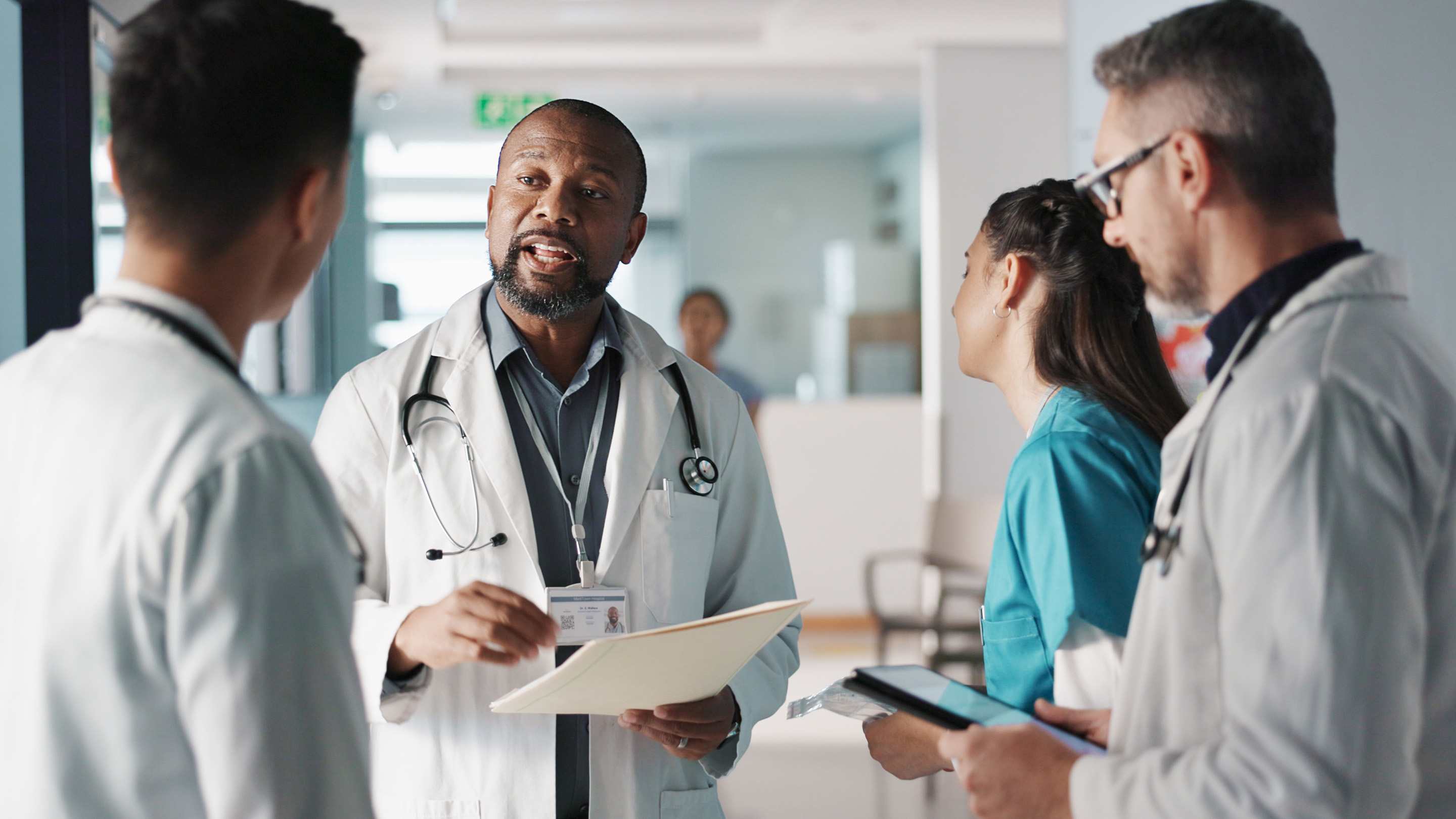 A faculty attending speaks to intern residents in the hallway of a hospital.