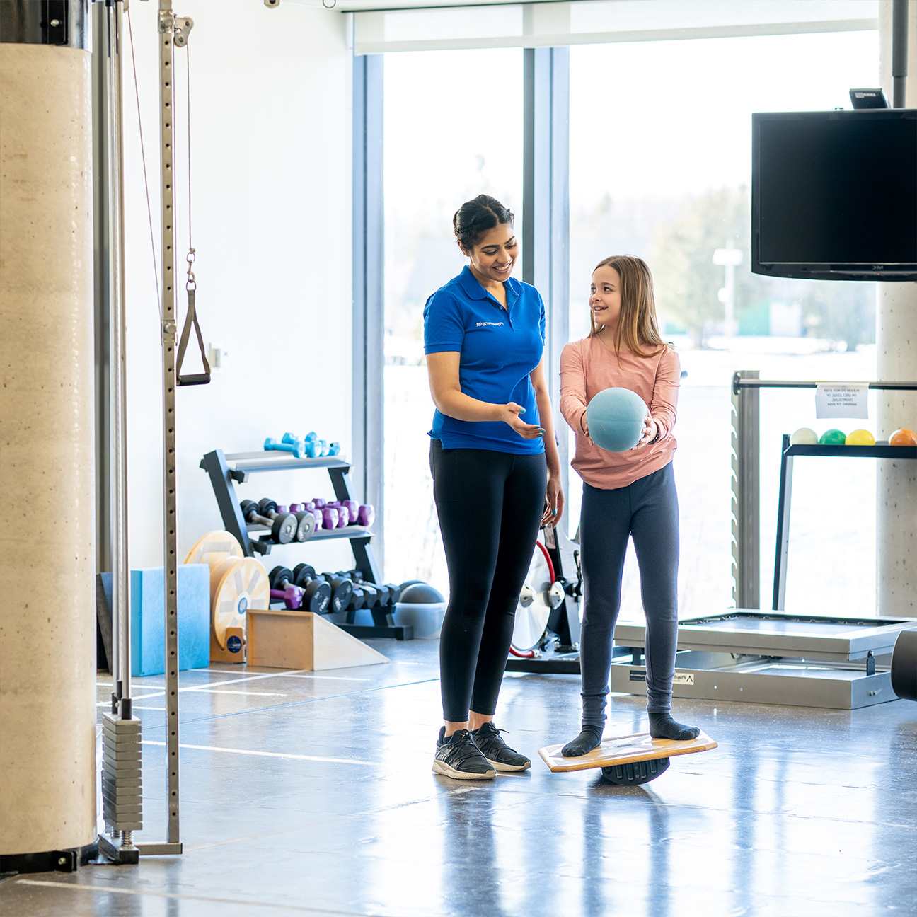 Woman works with young girl during physical therapy session.